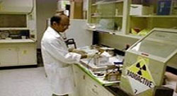 image of Medical, Industrial, and Academic Uses of Nuclear Materials and Agreement States with a person wearing a lab coat working with equipment next to a sign that says 'Radioactive'