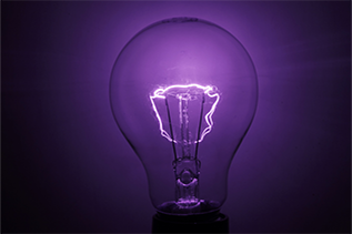Photo of an incandescent light bulb with a purple glow and a white glowing filament image on a black, rectangle background; the image represents the 'Innovation' Transformation Focus Area.