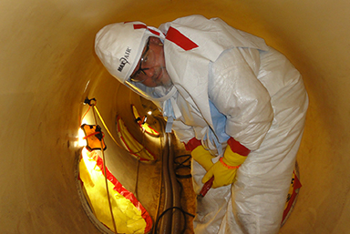 photo of a NRC employee overseeing repairs wearing a hazmat suit and face shield.