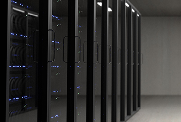 Image of computer server room with twelve large tall black servers with small blue lights sitting on a grey floor.