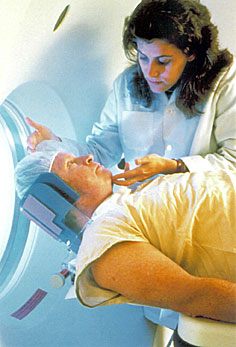 photo showing a man being prepped for a CT scan, being assisted by a female technician