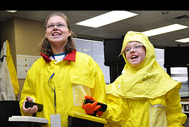 Image of two young girls in yellow protective coats holding remote controls.