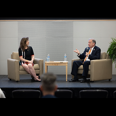 Image of two people sitting in chairs speaking into microphones. 