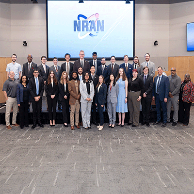 A large group of professionally dressed adults pose for a group photo in an auditorium.