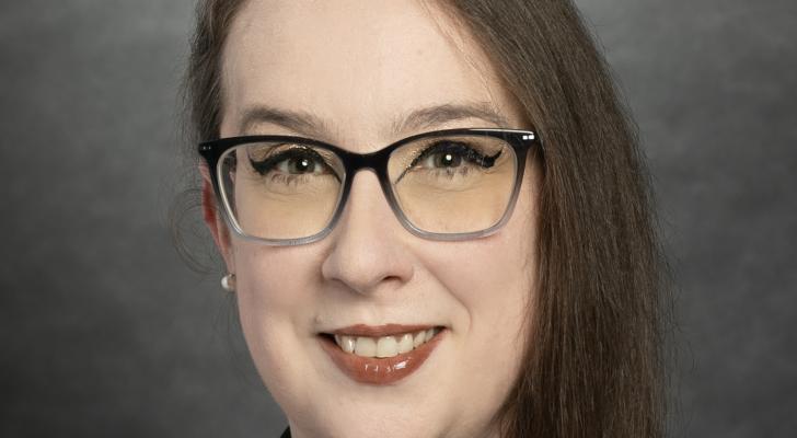 Profile picture of a white woman with long brown hair, glasses, and red lipstick