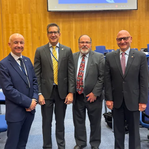 Image of four men in a large room smiling at the camera. 