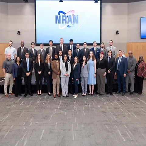 A large group of professionally dressed adults pose for a group photo in an auditorium.